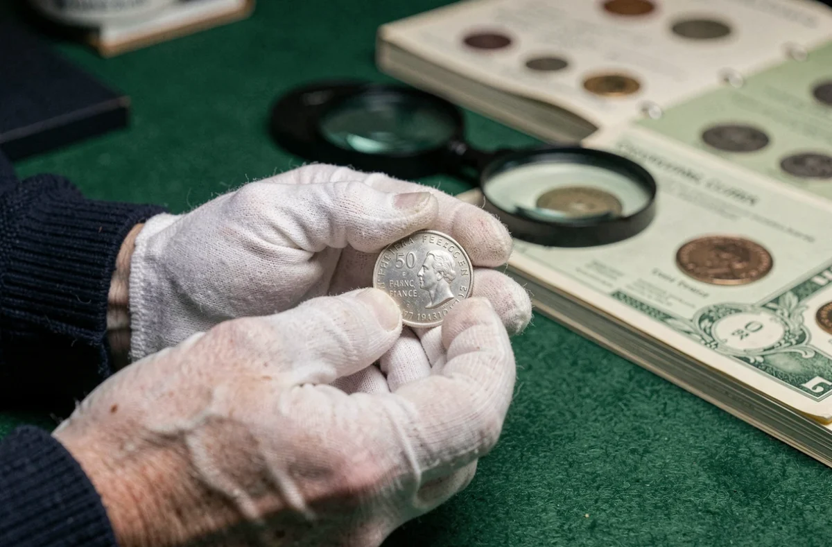 Collectionneur tenant une pièce de 50 francs 1977 avec des gants blancs sur bureau de numismate